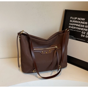 Detail view of dark brown tote bag featuring gold studs and exterior zipper pocket