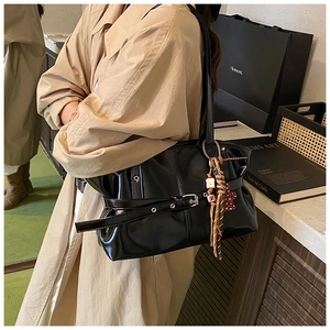 Détail d'un sac bandoulière noir brillant avec boucle décorative et pendentif coloré