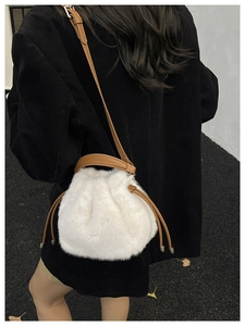Détail du sac seau en fausse fourrure blanche avec bandoulière en cuir sur veste noire