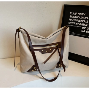 Detail of hobo bag featuring beige suede, brown leather trim, and gold rivet accents