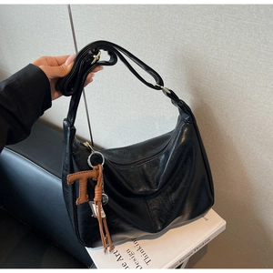Détail du sac hobo noir à texture litchi avec pendentif T et bandoulière réglable