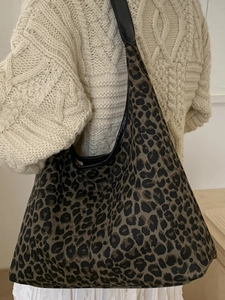 Chic leopard print oversized tote bag with black leather straps worn over a cream sweater