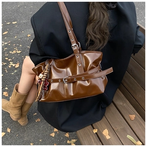 Détail d'un cabas marron foncé brillant avec sangles métalliques et breloque florale