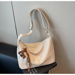 Détail du sac cabas beige montrant la texture du cuir PU et le pendentif lettre T marron