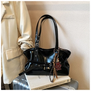 Détail du sac à bandoulière noir brillant avec sangle à boucle et charm ours sur valise