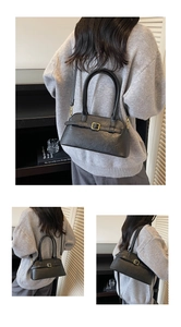Detail of a minimalist black leather shoulder bag with gold buckles and fixed handles