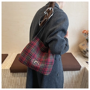 Dettaglio della borsa a tracolla tartan rossa con ciondolo a fiocco dorato su cappotto