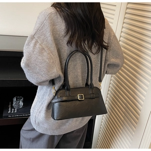 Detailed view of black textured leather shoulder bag with gold buckle on model