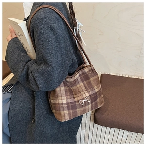 Dettaglio borsa a tracolla in lana scozzese marrone con fiocco d'argento indossata su cappotto