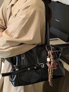 Sac à bandoulière plissé noir minimaliste avec charms porté par un mannequin en trench