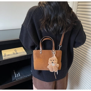 Brown faux suede bucket bag with a teddy bear charm shown on model in retro casual style
