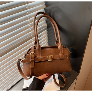 Close-up of caramel leather shoulder bag showing buckle straps and gold-tone metal hardware