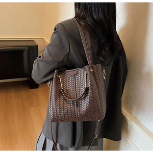 Detail of dark brown woven leather tote with metallic handle and textured finish