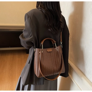 Detail of a large brown woven leather bucket bag worn by a model in a stylish interior