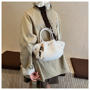 Detail of white plush bucket bag with round handle and wooden bead charm on a model
