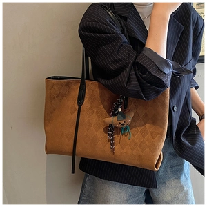 Macro detail of caramel brown tote bag featuring quilted texture and cute bear pendant