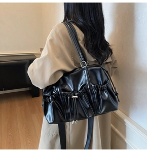 Detail view of the black glossy pleated shoulder bag with decorative drawstring accents