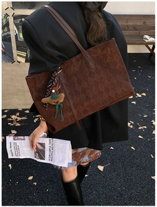 Detail of dark brown quilted suede tote bag with a cute bear charm for autumn style