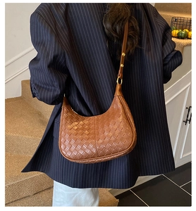 Close-up of brown woven leather crescent shoulder bag on model with striped blazer