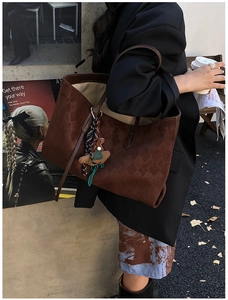 Detail view of brown woven texture tote bag with teddy bear charm in urban street setting