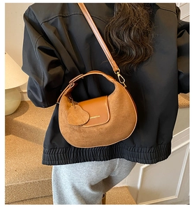 Detailed side view of a brown crescent shoulder bag with heart charm and leather strap