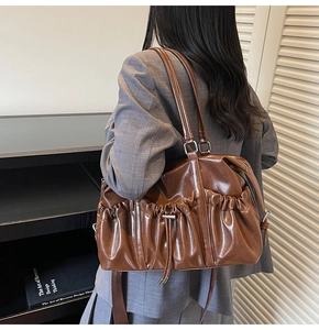 Brown vintage pleated tote bag with drawstring detail worn as a stylish shoulder bag