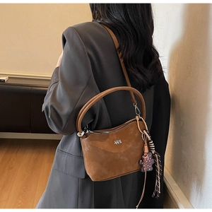 Detail view of brown suede bucket bag with bear charm and checkered ribbon decor