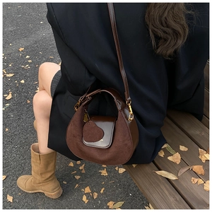 Detail of dark coffee crescent bag with heart charm shown in an autumn street setting