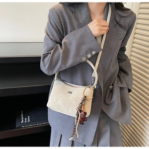Detail of a creamy white soft leather bucket bag with a cute bear and tassel charm