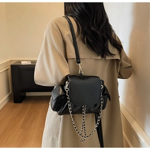Detail showing glossy black chain shoulder bag with quilted texture and side pockets