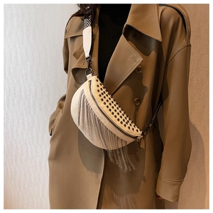 Detail of cream crossbody bag featuring black rivets and metallic silver fringe tassels