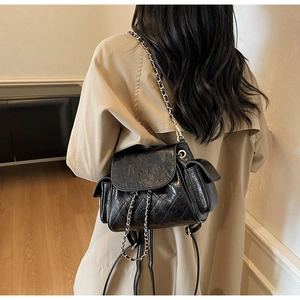 Detail of black quilted leather backpack with chain straps and side flap pockets on a model