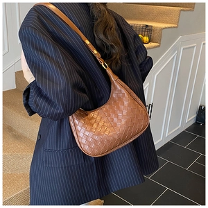 Brown woven leather moon bag detail shown with a dark blue blazer in an indoor setting