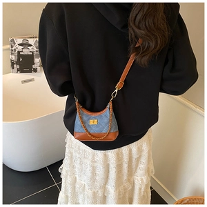 Detail view of mini denim crossbody bag with brown leather trim and golden chain strap