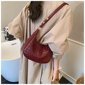 Detailed close-up of woven burgundy crescent leather bag with golden ring hardware