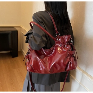Model wearing dark red glossy shoulder bag with functional side drawstrings and pockets