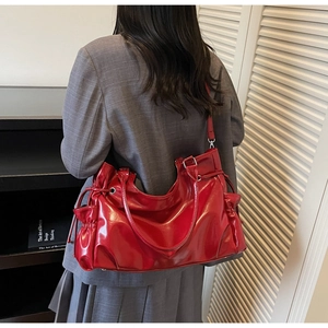 Detail view of red glossy shoulder bag with drawstring pleats and silver buckle on strap