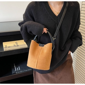 Brown frosted suede bucket bag with black leather handle shown in a modern lifestyle setting