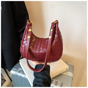 Detail of burgundy woven hobo bag with gold hardware rivets on elegant silver luggage