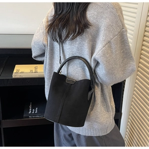 Detail shot of the matte suede texture and handle on a minimalist black bucket bag