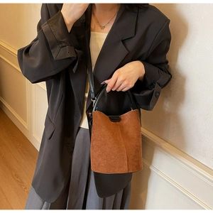 Detail view of brown matte bucket bag with black leather handle and shoulder strap