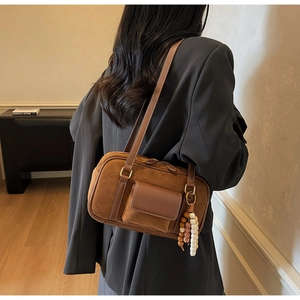 Detail of vintage brown suede shoulder bag with retro beaded charm in a warm home setting