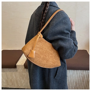 Détail d'un sac d'épaule en daim marron au design d'arc asymétrique sur modèle