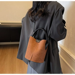 Close-up of brown suede bucket bag featuring black leather trim and embossed brand logo