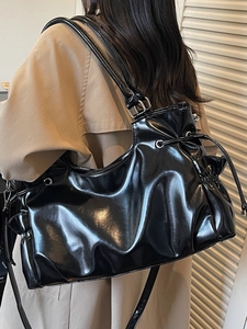 Minimalist black patent leather tote bag with side drawstrings shown on a female model