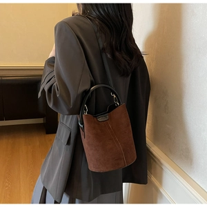 Brown suede bucket bag with vertical stitching shown being worn by a model in a gray blazer