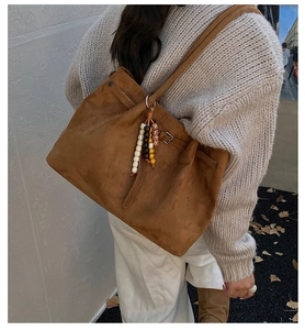 Detail der braunen Wildleder-Tote-Bag mit Boho-Perlen-Quaste am Strickpullover