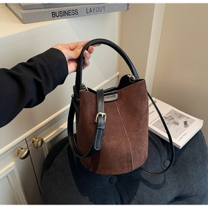 Close-up of brown matte suede bucket bag with black leather strap on a velvet cushion