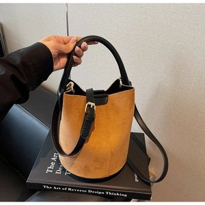 Detail of brown suede bucket bag with black leather handle and gold hardware accents