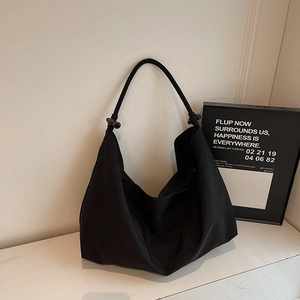 Detail einer minimalistischen schwarzen Hobo-Bag mit Knotengurt und brauner Holzperle
